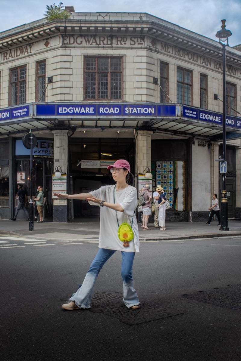 East Asian woman in karate pose in front of Edgware Rd tube station